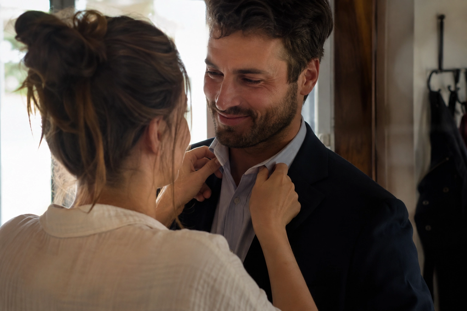 Una donna sistema il colletto della camicia a un uomo in giacca mentre lui la guarda sorridendo